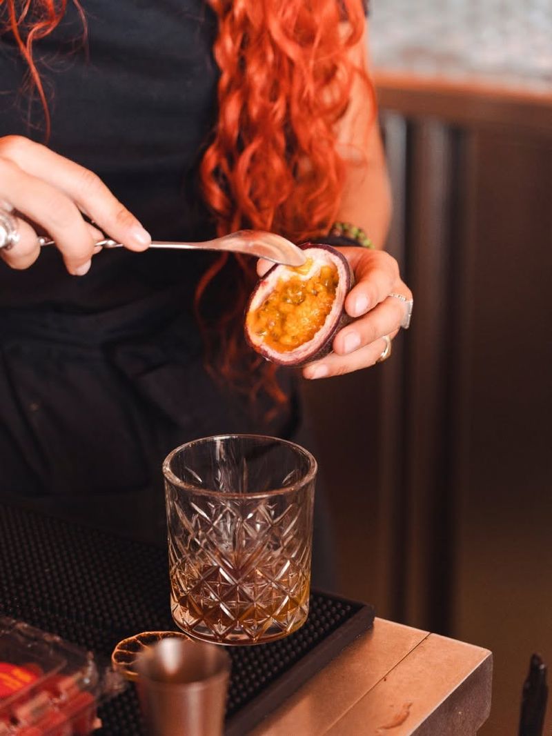 A bartender spooning passion fruit into a cut-glass tumbler