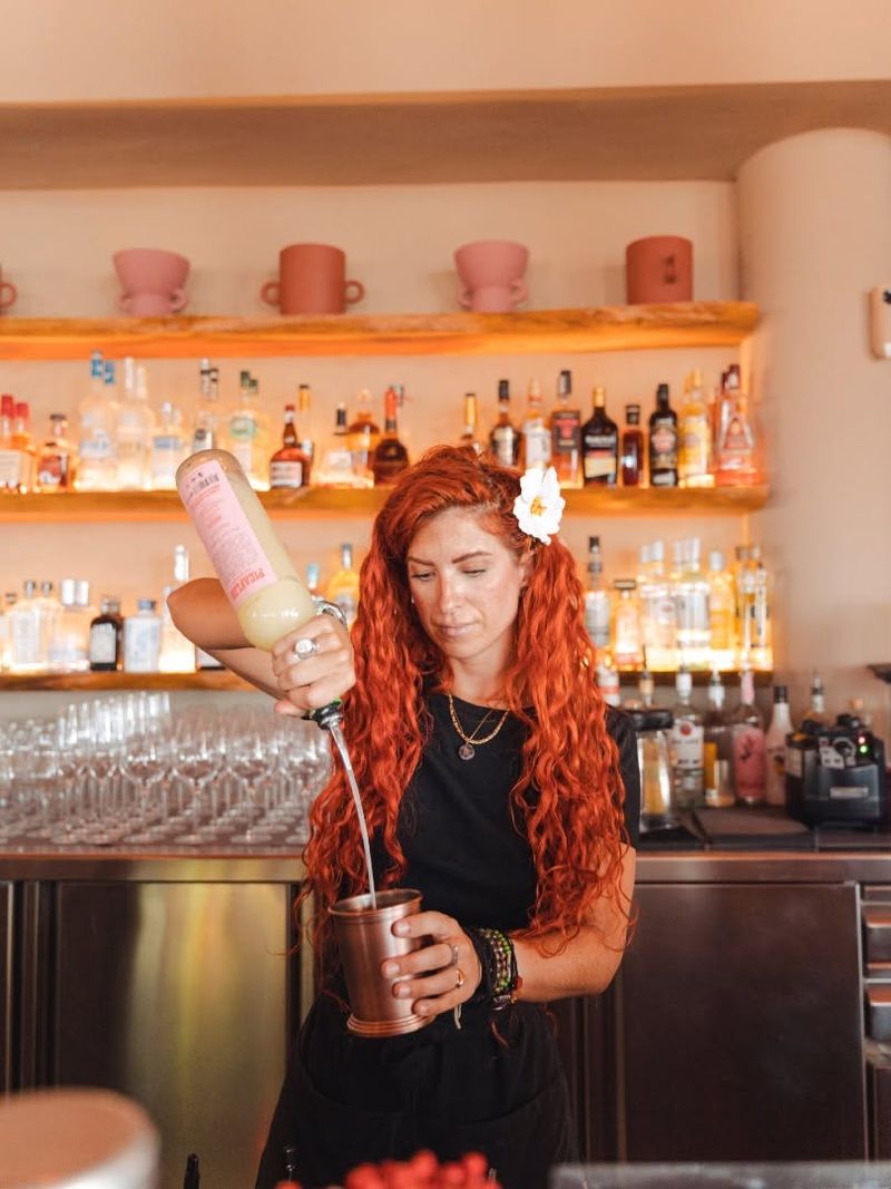 A bartender pouring a cocktail in front of the backlit bar shelves