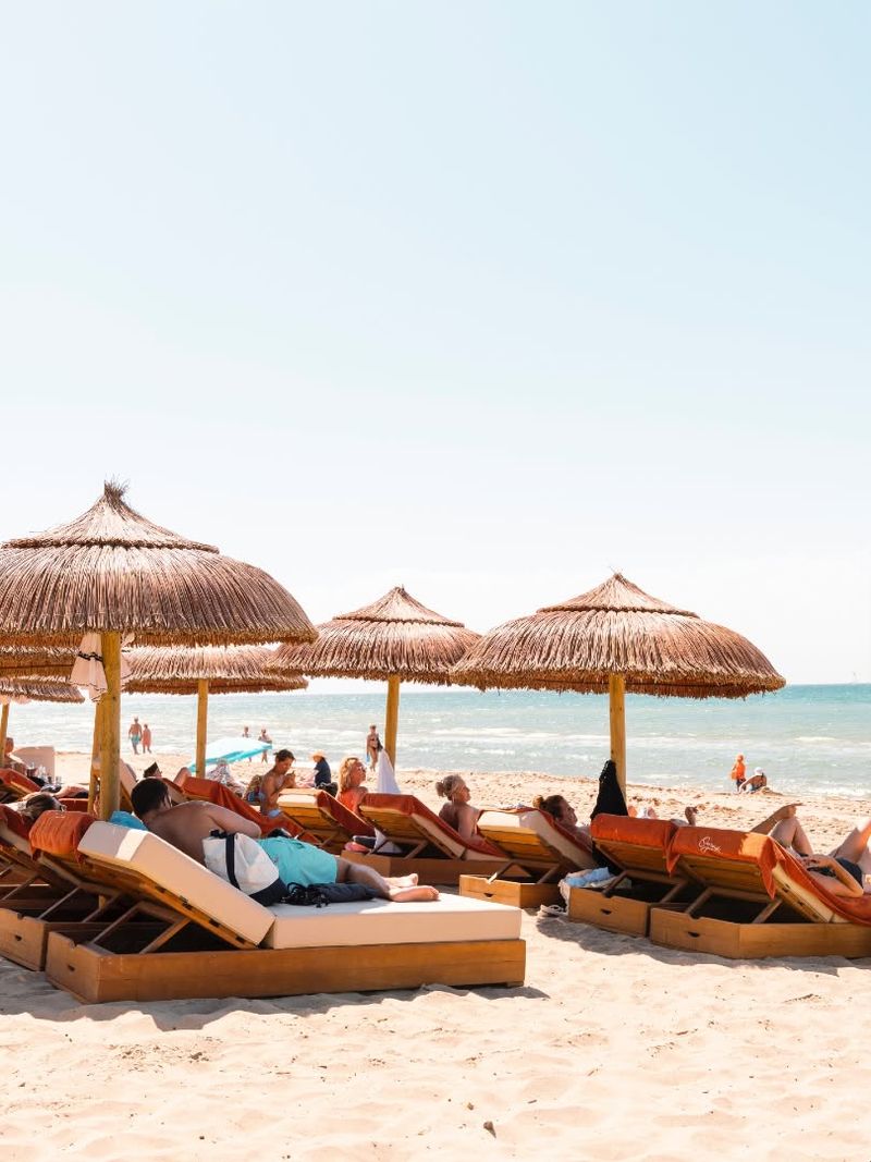 Guests on sunbeds beneath thatched parasols beside the sea