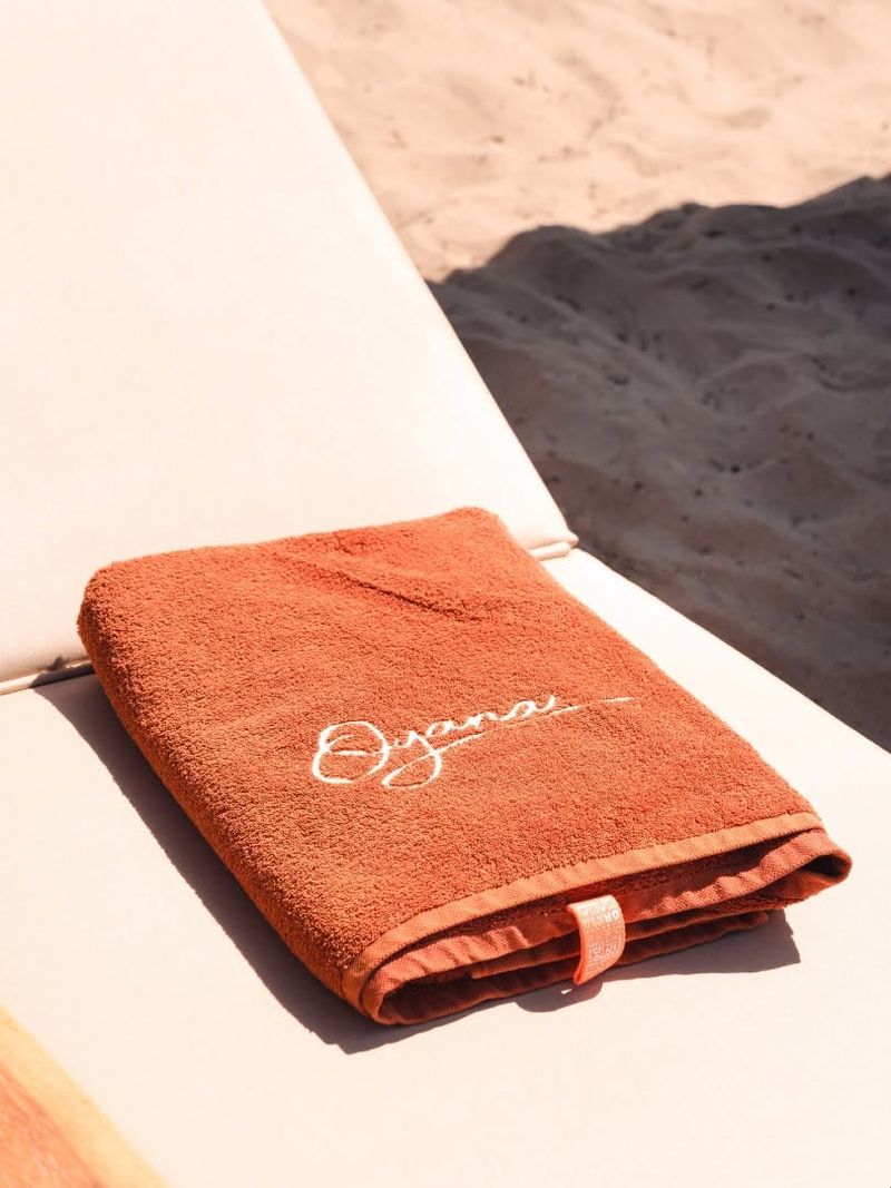 A rust-coloured Oyana towel folded on a sunbed