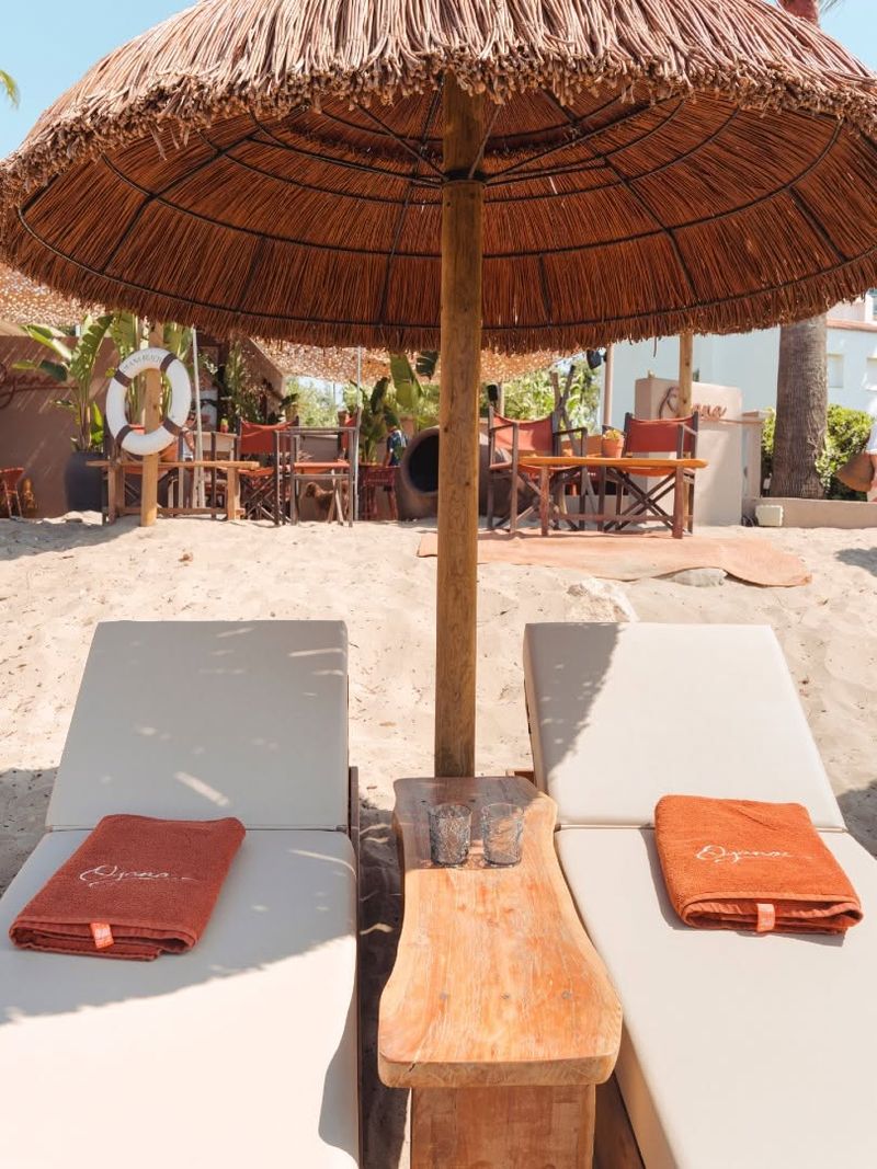 Two sunbeds with Oyana towels either side of a wooden side table under a parasol