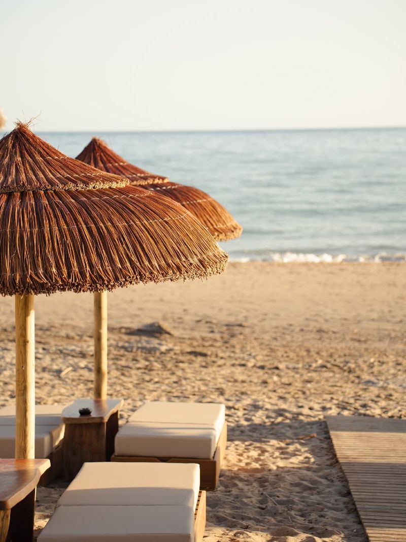 Thatched parasols and cream sunbeds on the sand facing the sea