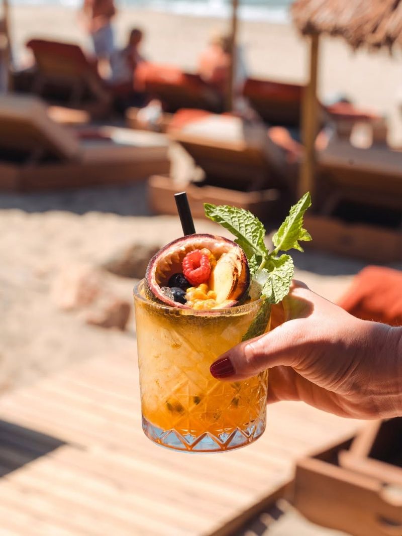 A passion fruit cocktail held up in front of the sunbeds