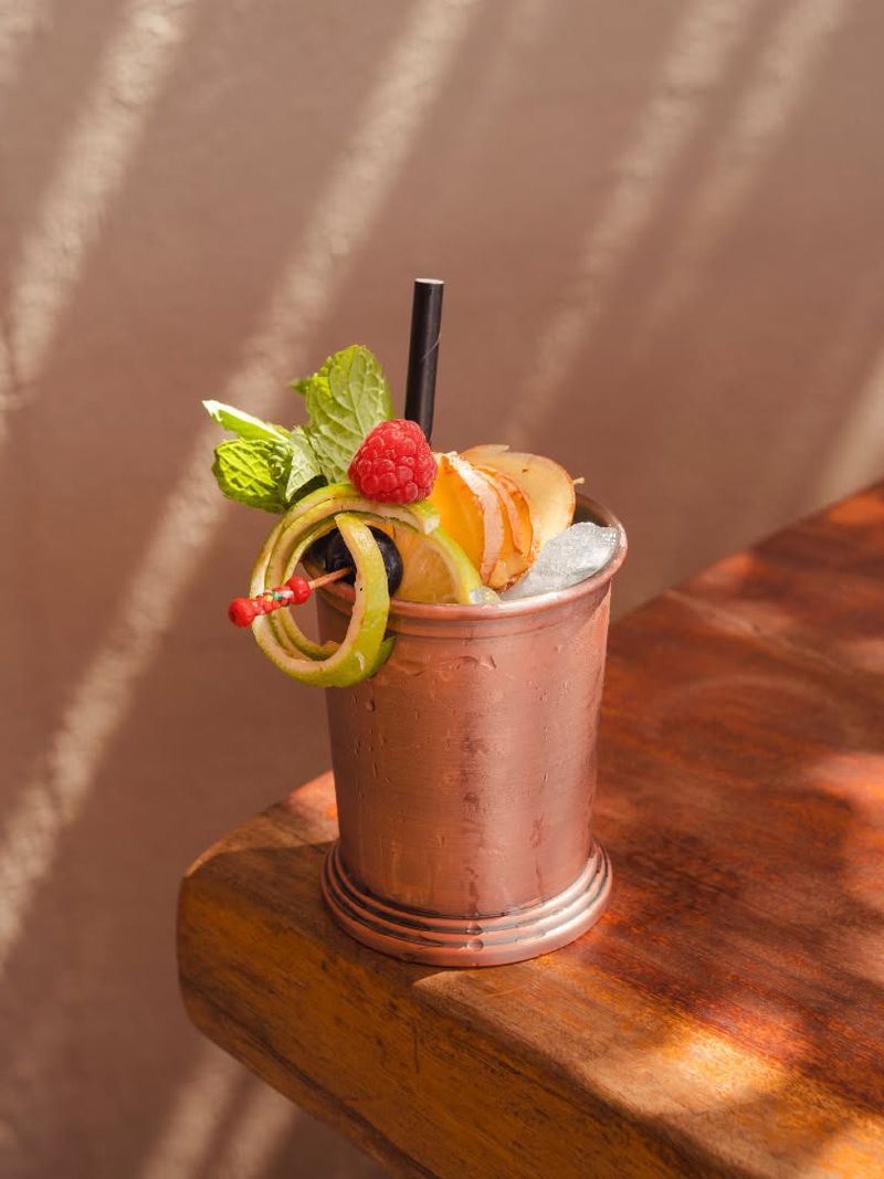 A cocktail in a copper cup garnished with fruit and mint