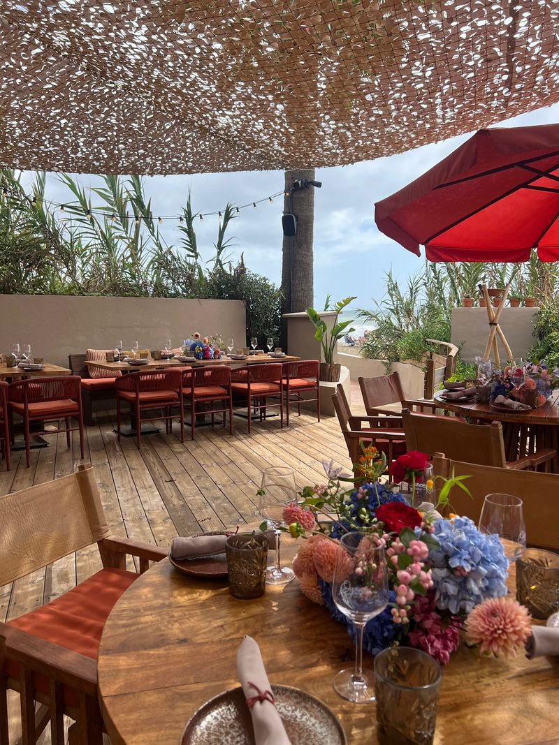 A terrace laid for a private lunch with flowers on round tables and red parasols