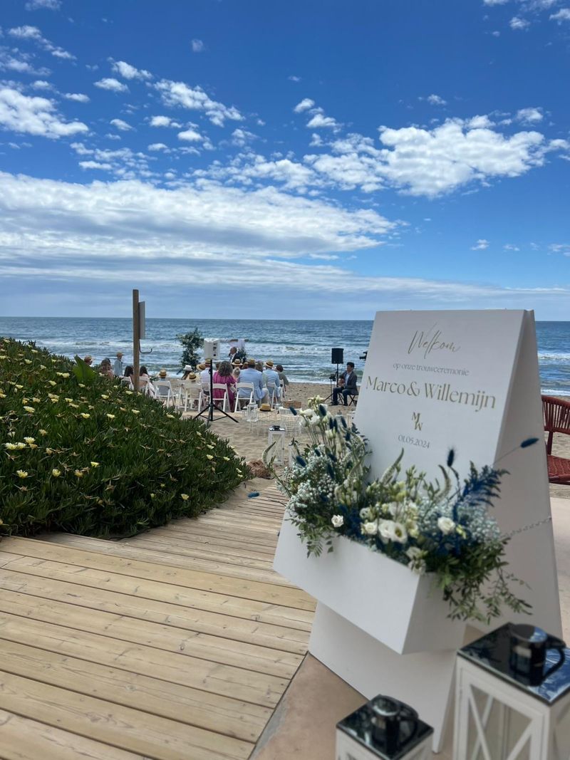 A floral welcome sign for a wedding on the boardwalk leading to the beach