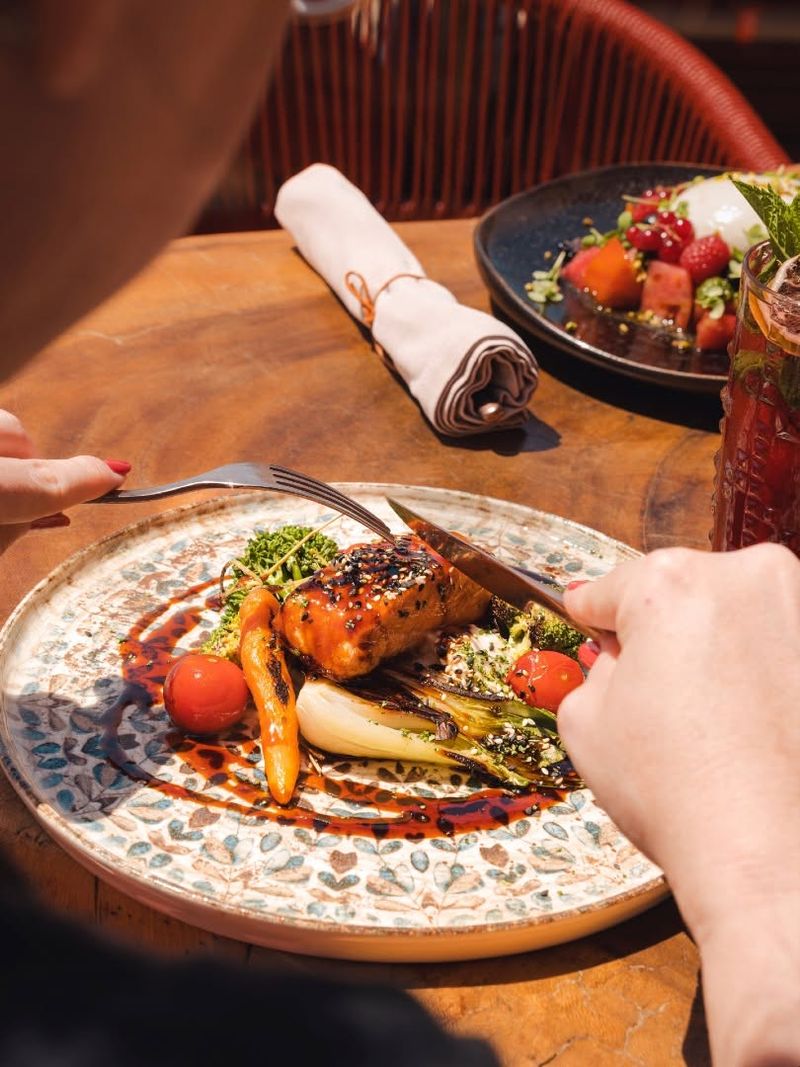A glazed salmon dish with grilled vegetables on a patterned plate