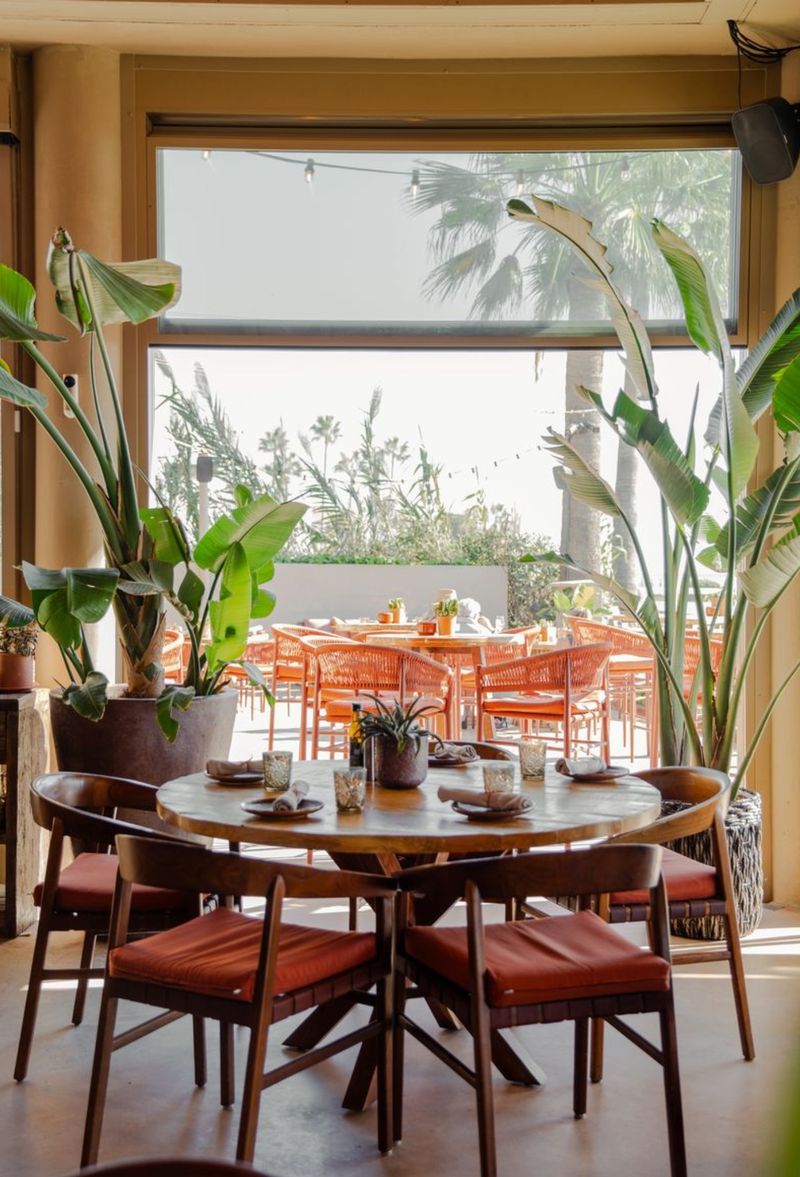 A round table set for lunch inside, with the terrace and palms visible through the open window